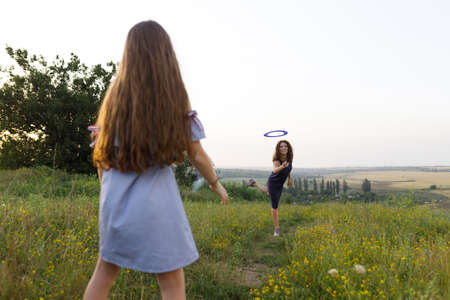 young red-haired mom and her red-haired daughter launch a throwing saucer outdoors during sunsetの写真素材