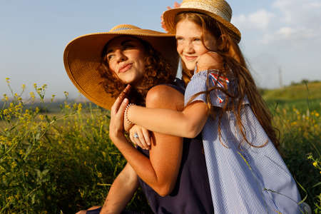 young mom and her wonderful daughter have fun outdoors wearing dresses and straw hats