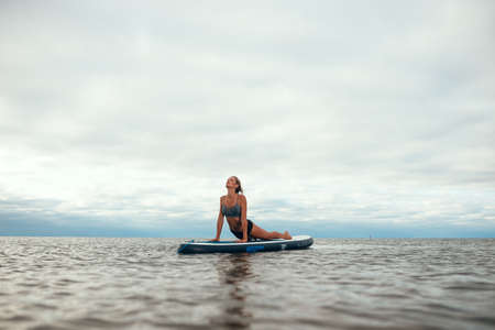 Woman practicing yoga on the paddle board in the morning. Photo without retouchingの写真素材