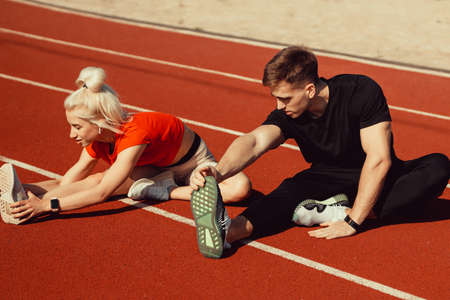 girl and a guy doing a warm-up before sports exercises at the school stadiumの写真素材