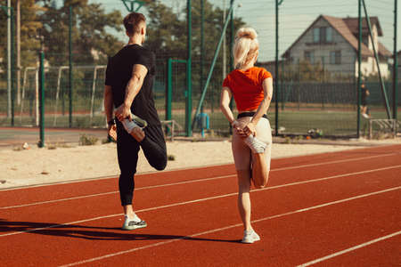 girl and a guy doing a warm-up before sports exercises at the school stadiumの写真素材