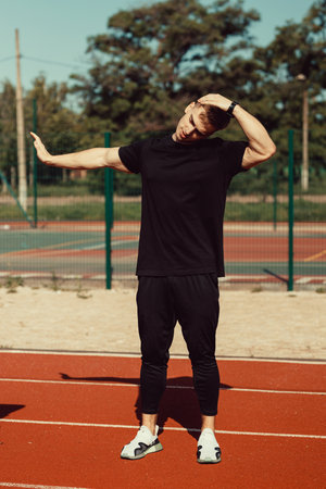 young guy doing warm-up before sports exercise at school stadiumの写真素材