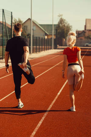 girl and a guy doing a warm-up before sports exercises at the school stadium