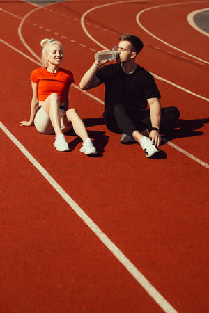 young beautiful blonde and a guy are sitting on a jogging track with a bottle of water and chattingの写真素材