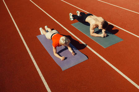 Young couple doing sports in the stadium lying on yoga matsの写真素材