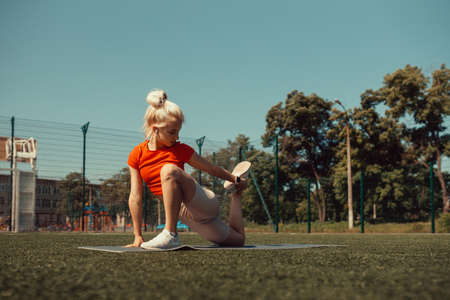 Beautiful blonde doing stretching on the lawn of a football fieldの写真素材