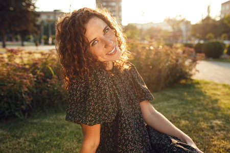 charming curly red-haired girl with freckles in dress poses for the camera in the city center showing different facial emotionsの写真素材