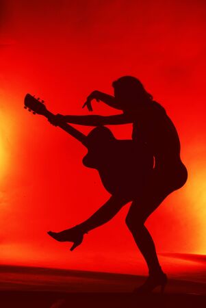 Woman with guitar silhouette on red background の写真素材