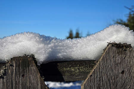 Wooden fence in winter with snow and ice crystals on topの写真素材