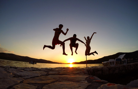 Silhouette of friends jumping at sunset on the beachの写真素材