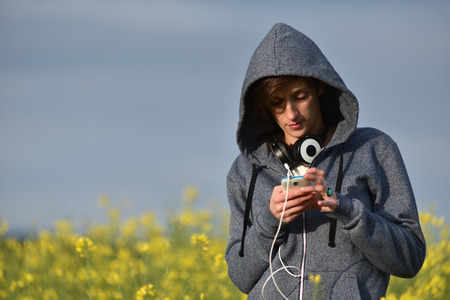 Young woman in hoodie texting a message on her smart phoneの写真素材