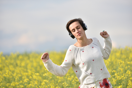 Young, emotional and happy woman listening music in headphones in a canola fieldの写真素材