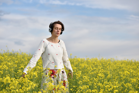 Young, emotional and happy woman listening music in headphones in a canola fieldの写真素材