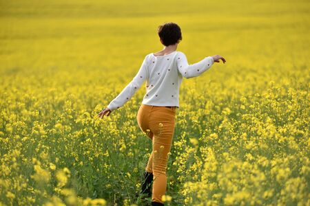 Hipster girl walking through a canola field. Freedom concept