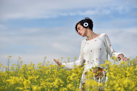 Sensual lady listening music in headphones and dancing in a canola fieldの写真素材