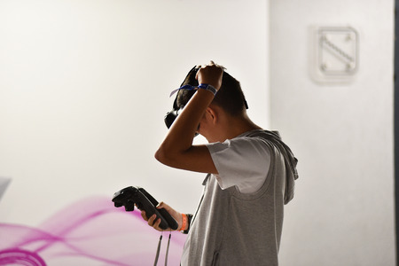CLUJ-NAPOCA, ROMANIA - AUGUST 5, 2016: Boy tries virtual reality HTC Vive headset and hand controls during the virtual reality exposition, at the Untold Festivalのeditorial素材