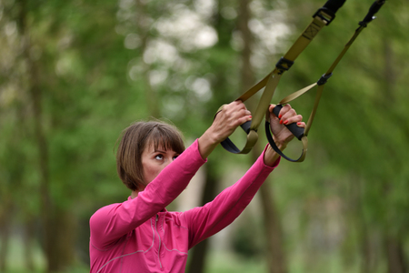 Woman doing arms biceps curl training with trx fitness straps in the outdoorsの写真素材