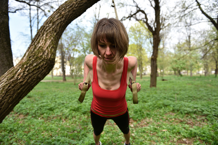 Young muscular woman does suspension training with fitness straps in the outdoors