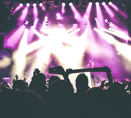 Crowd of audience with hands raised at a music festival. Lights streaming down from above the stageの写真素材