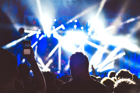 Crowd of audience with hands raised at a music festival. Lights streaming down from above the stageの写真素材