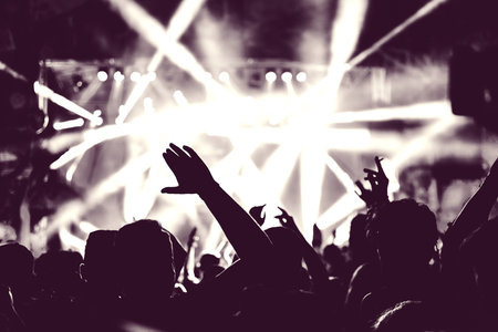 Crowd of audience with hands raised at a music festival. Lights streaming down from above the stageの写真素材