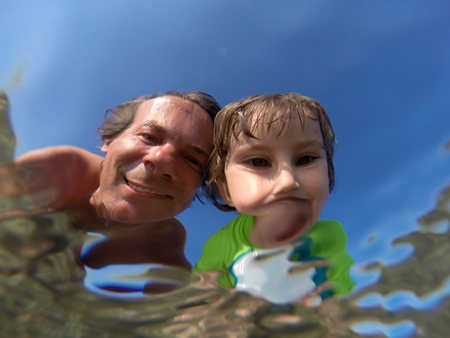 Father and her toddler daughter having fun at the sea. Distorted faces view through water, underwater viewの写真素材