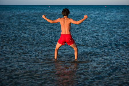 Slim guy posing in red swimwear in sea water. Parody conceptの写真素材