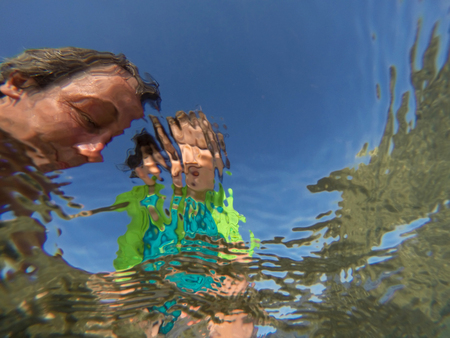 Father and her toddler daughter having fun at the sea. Distorted faces view through water, underwater viewの写真素材