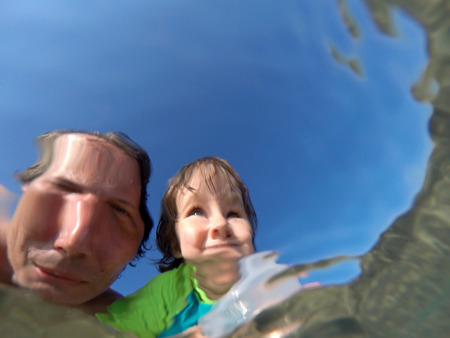 Father and her toddler daughter having fun at the sea. Distorted faces view through water, underwater viewの写真素材