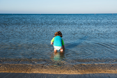 Cute toddler baby playing in shallow sea waterの写真素材