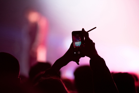 Silhouette of hands recording a concert with smart phones. Crowd of people using smart phones to...