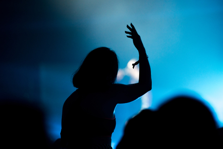 Rear view of crowd with arms outstretched at concert. Bright stage lights in the backgroundの写真素材