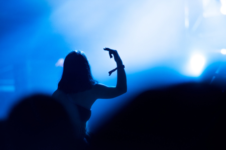 Rear view of crowd with arms outstretched at concert. Bright stage lights in the backgroundの写真素材