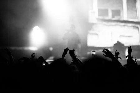 Rear view of crowd with arms outstretched at concert. Bright stage lights in the backgroundの写真素材