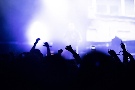 Rear view of crowd with arms outstretched at concert. Bright stage lights in the backgroundの写真素材