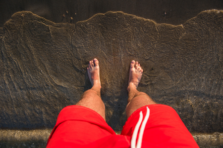 Man's feet in the sand, sea waves approaching beachの写真素材