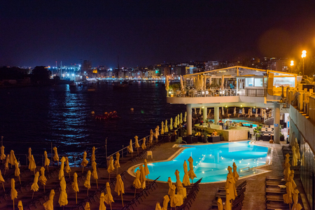 SLIEMA, MALTA - AUGUST 22, 2017: Tourists relaxing near a sea luxurios swimming pool at night with a great panoramic night cityscape to Vallettaのeditorial素材