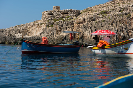 BLUE GROTTO, MALTA - AUGUST 23, 2017: Tourists taking a boat trip at the Blue Grotto. The sea caves of Blue Grotto and natural arch are one of the major tourist sights of Maltaのeditorial素材
