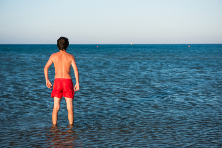 Slim guy posing in red swimwear in sea water. Parody conceptの写真素材