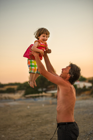 Father and his daughter having fun at the beach during summer holiday vacation. Man throwing his baby girl in air at beachの写真素材