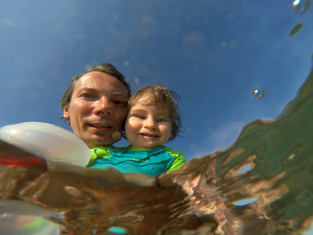 Father and her toddler daughter having fun at the sea. Distorted faces view through water, underwater viewの写真素材