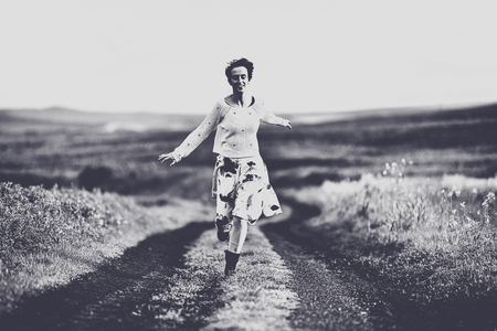 Woman in skirt running on a countryside road. Freedom concept. Black and white, toned, vintage effectの写真素材