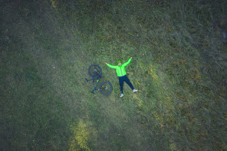 Aerial drone view of a cyclist lying down and resting in a meadow