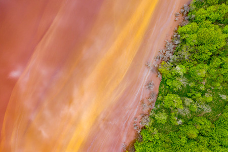 Aerial view of colorful red copper mining waste water in contrast with fresh green forest by droneの写真素材