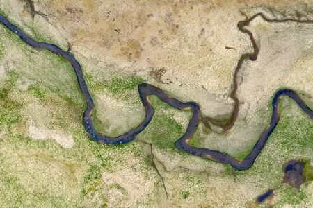 Winding water stream meandering on a meadow, Iceland. Aerial drone view