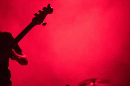 Silhouette of a musician playing on a bass guitar in red stage lightsの写真素材