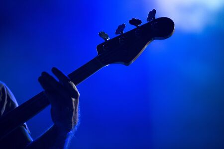 Silhouette of a musician playing on a bass guitar in blue stage lightsの写真素材