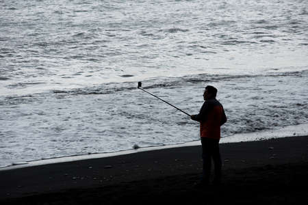 VIK, ICELAND - MAY 21, 2019: Tourist visiting the Reynisfjara beach and taking selfie on the Atlantic coast of Southern Iceland in Vikのeditorial素材