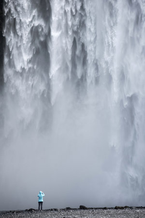 Traveler woman admiring Skogafoss waterfall, in Southern Iceland, one of country's most epic tourist destinationsの写真素材