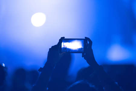 Hand holding smart phone and recording photo or video. Concert crowd and lights in backgroundの写真素材